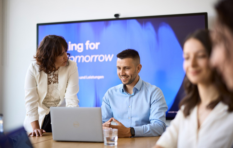 2 Mitarbeitende unterhalten sich vor Working for your tomorrow Schriftzug