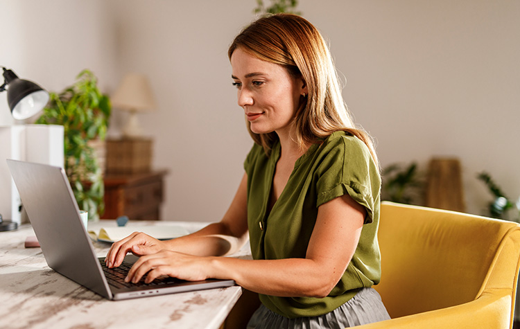 Eine blonde Dame arbeitet an Ihrem Laptop.